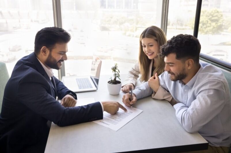 A mortgage broker advises a young couple in his office. 