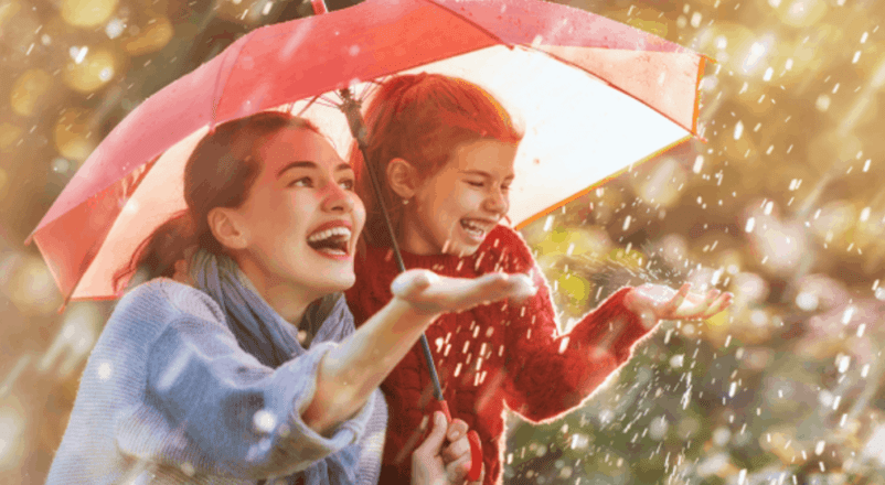 Mother and daughter laughing under an umbrella in the rain