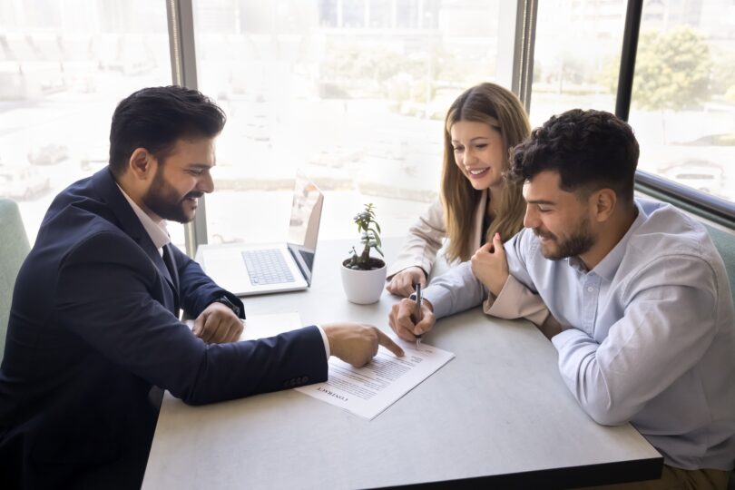A mortgage broker advises a young couple in his office.